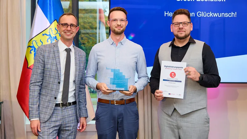 Digitalisierungsminister Dirk Schrödter steht mit Cedrik Hoffmann und einem Vertreter von PROGEEK vor einer Leinwand mit der Aufschrift „Green Ecolution, Herzlichen Glückwunsch!“. Cedrik Hoffmann hält in der Mitte die gläserne Trophäe, rechts neben ihm wird die Urkunde gezeigt.