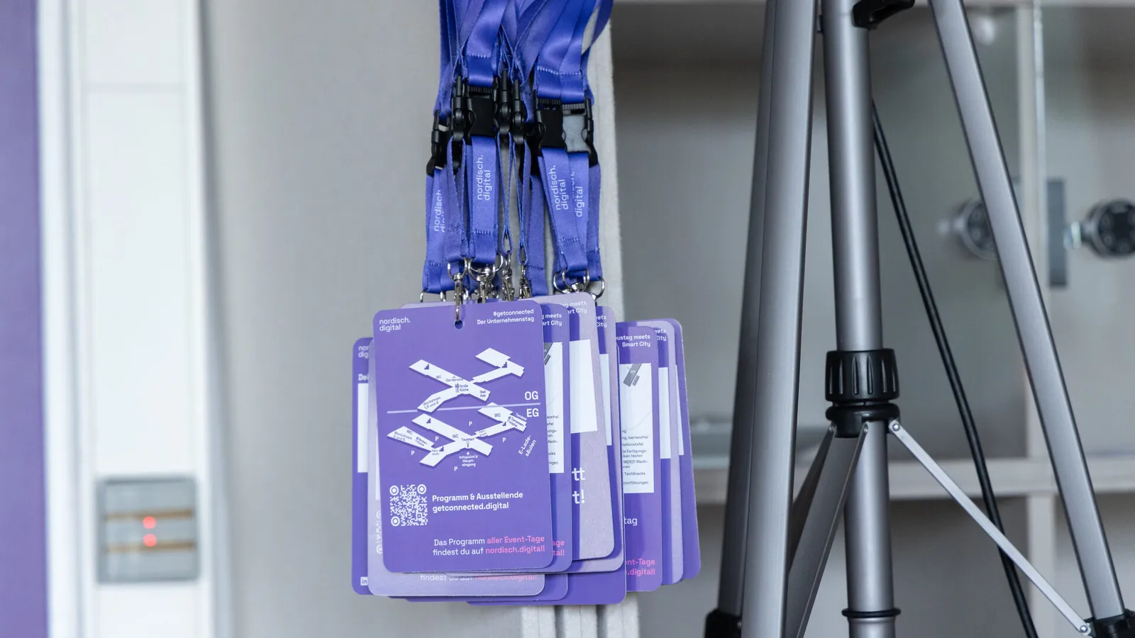 Lila Namensschilder der nordisch.digital hängen an Lanyards an einer Wand