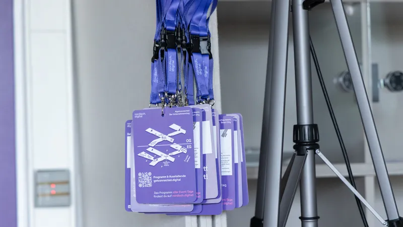 Lila Namensschilder der nordisch.digital hängen an Lanyards an einer Wand